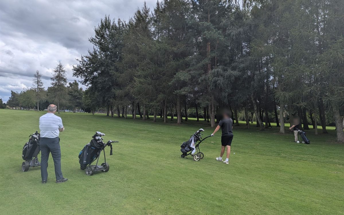 Players with their trolleys on a tree-lined fairway